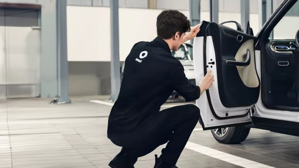 Person squatting and inspecting the inside edge of an open car door in a garage or workshop setting